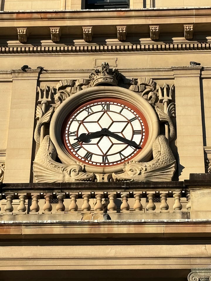 Detail of the large ornamental clock with decorative eel-like fish on either side. A picture of the Customs House facade with building entrance.