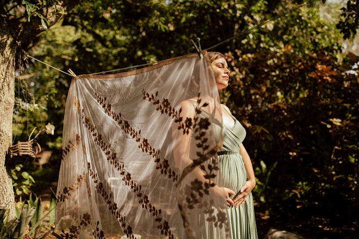 Four photos in shades of greens and coppers and gold, depicting Ganga Devi 6 months pregnant in a sage green gown surrounded by copperleaf plants and gold brocade fabric. In the background of the final photo, etched glass reads the lines from Stanley Kunitz: "The Universe is a continuous web, touch it at any point and the whole web quivers.""