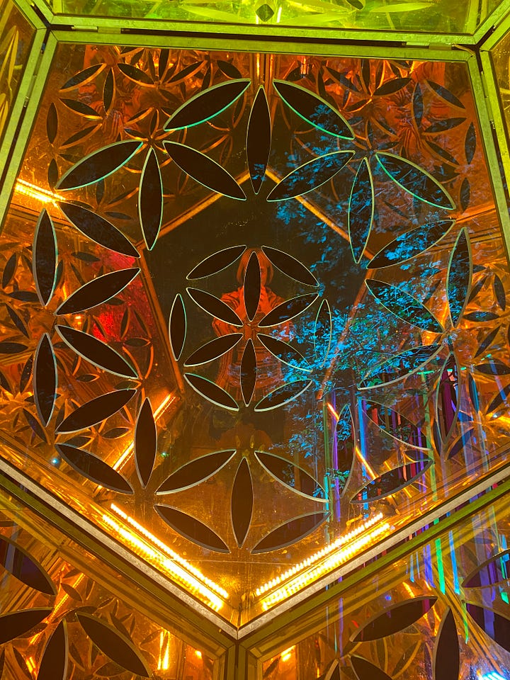 Artistic lighting at latitude festival (large latitude letters in a reflective metal lit up, multi-coloured strips leading into the zen area lit up with giant brightly coloured flowers leading to the entrance, lights strung up between trees in the wood and finally a kaleidoscope dome in gold