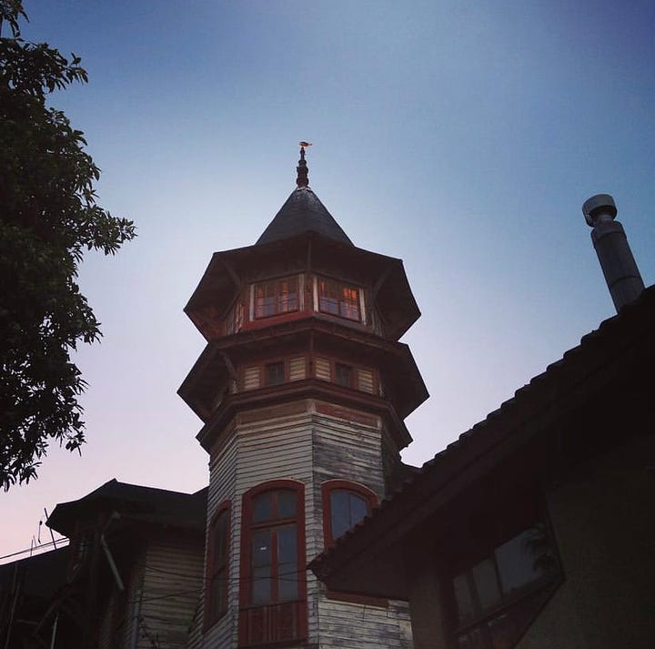 A victorian touret glows during sunset in Playa Ancha while two  stylish men chat in front of Baburizza Palace. 