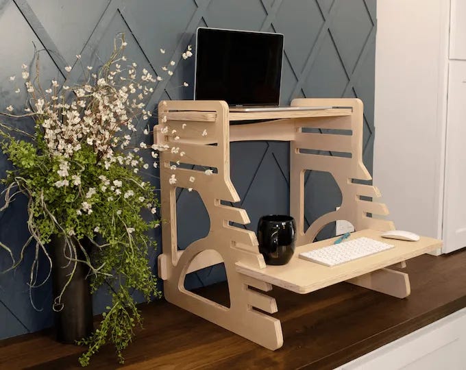 Two standing desks; the white one is electric, the wooden one, surrounded by plants, is modular. 