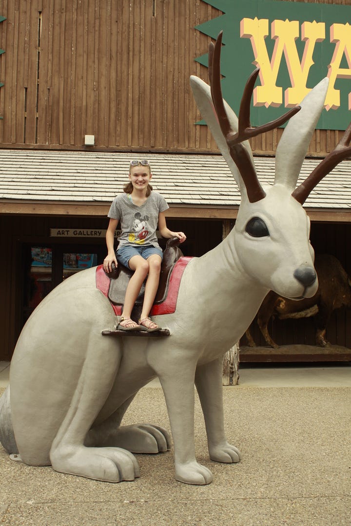 A photo of a girl on a statue of a jackalope, two photos of a boy and a girl getting cups of water, and a boy drinking water from a cone shaped cup.