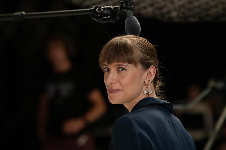 A white woman with bangs and earings smiles at the camero over her shoulder.