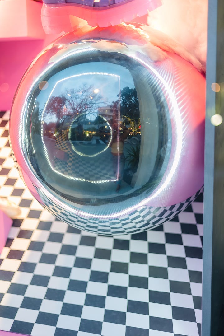 Image of a reflective surface with a round display case for art in a store; photo of a reflective surface overlaid on an outdoor dining and patio scene in a shopping area, with two people walking and superimposed on the background.