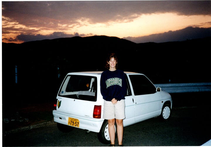 An image of me, smiling and young, driving a car with its steering wheel on the righthand side; and another image of me standing in front of a small, white hatchback at sunset. 