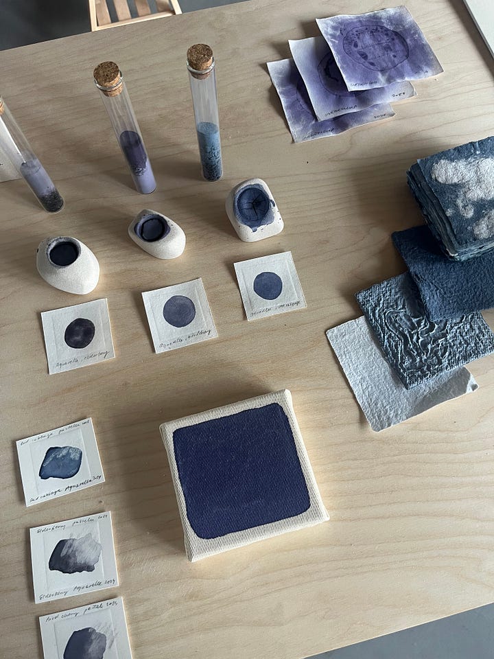 1-2. Exhibition table for 'blues' from Slow Painting Studio showing samples of blue paints on paper derived from kitchen food waste scraps.
