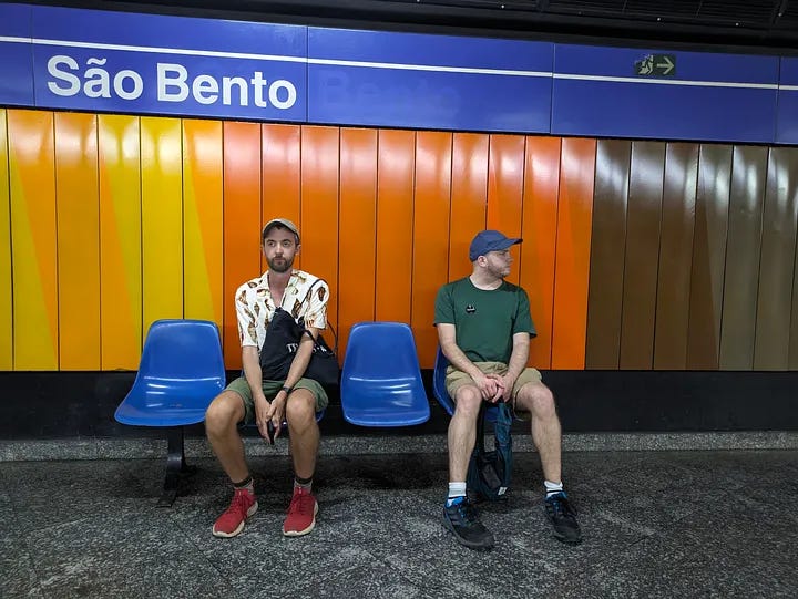 A church in São Paulo, one traveler smiling next to a man's portrait, two travelers waiting for the subway, and all three travelers smiling in a bar and toasting beers