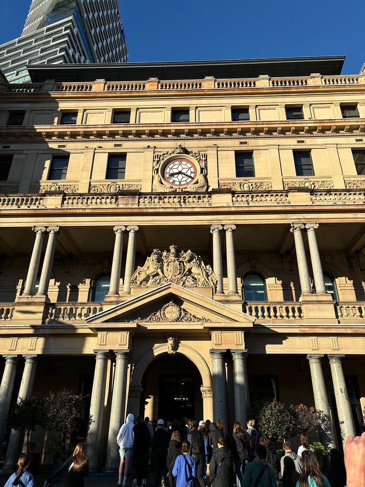 Detail of the large ornamental clock with decorative eel-like fish on either side. A picture of the Customs House facade with building entrance.