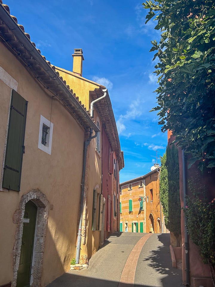 Karen Bussen stands next to a door in Provence, and scenes of a pretty street and pastel stone houses in Provence