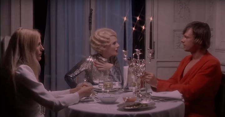 left: A still from Daughters of Darkness where a blonde in a silver sequin gown sits with a man in a red robe to her left and his blonde wife sits to her left. They are at a table with silver servwear and tall candlesticks. On the right, a brown-haired woman in a silver sequined dress sits between a blond woman (to her right) and her husband (to her left), they all sit at a dinner table with silver platters and tall candlesticks.