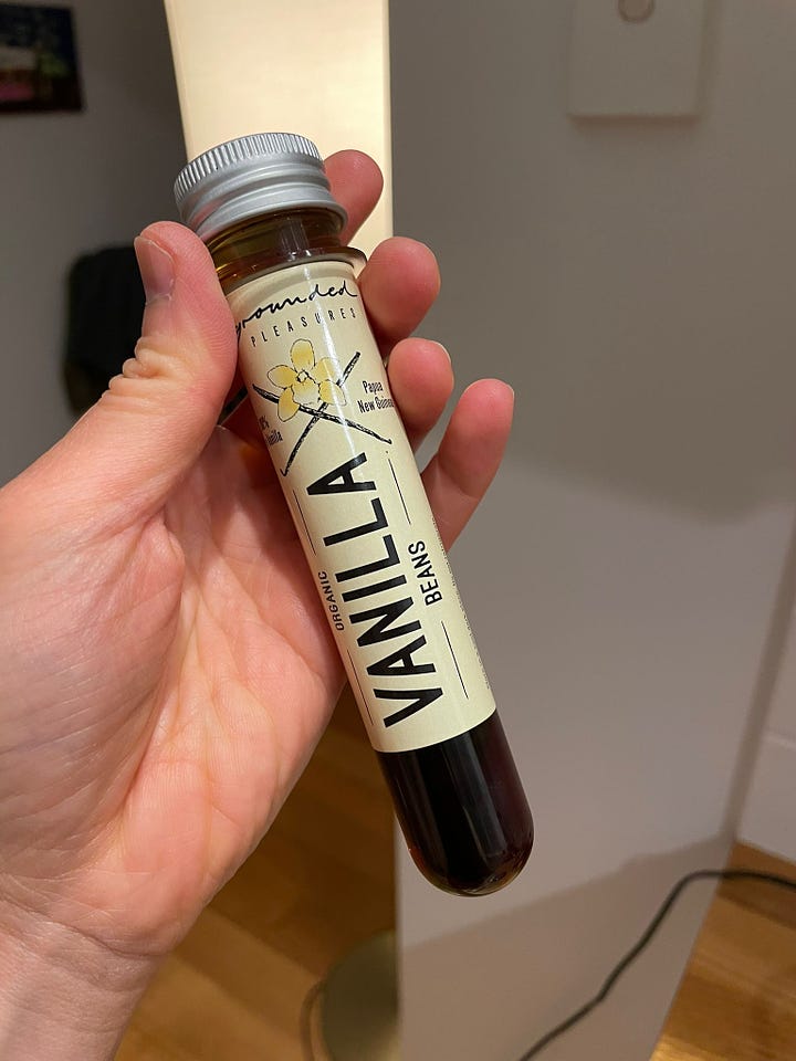 A test tube with vanilla beans and vodka, making homemade vanilla extra. A hand holds a small bottle of vanilla extract, decanted from the test tube.