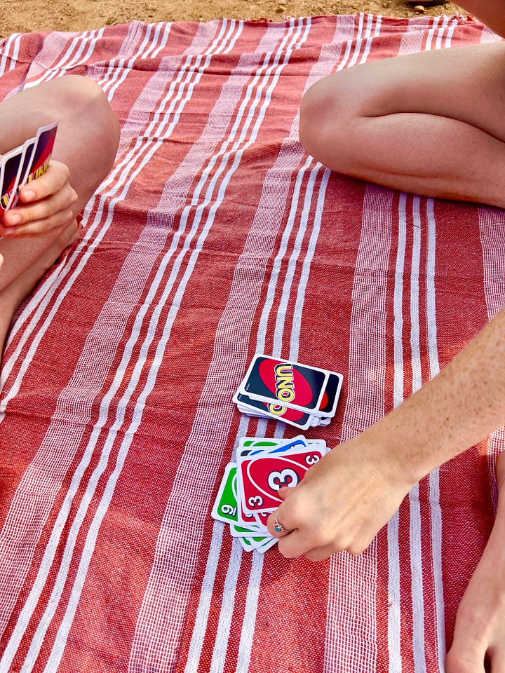 The first image on the left is of Sawyer Wilson, who is a freelance copywriter, in Menorca wearing a linen dress. The second image on the right is of hands holding UNO cards in the middle of a game, while the players sit on a red striped towel.