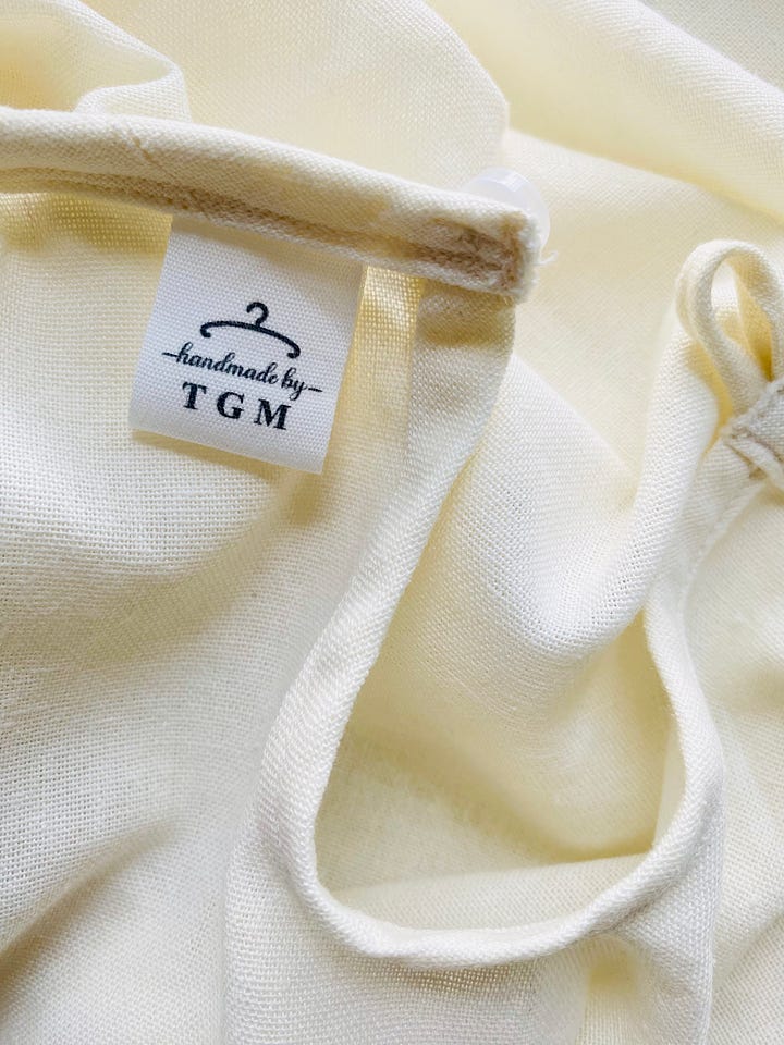 Left image of 4 fabric tags on a wooden table. Fabric tags read "handmade by TGM". Right image of fabric tag sewn into shirt collar.