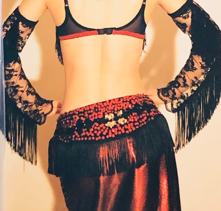 Fringe, coins, sequins and lace. A shot of my hips in a spangly red belly dance belt, and posed on the floor in blue-and-black, one arm and gaze uplifted, light and focus back in my eyes.