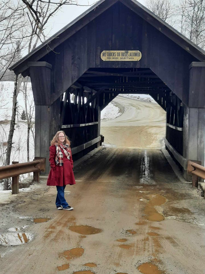 Amber poses at a brown wooden covered bridge, the dirt road is covered in mud and potholes.