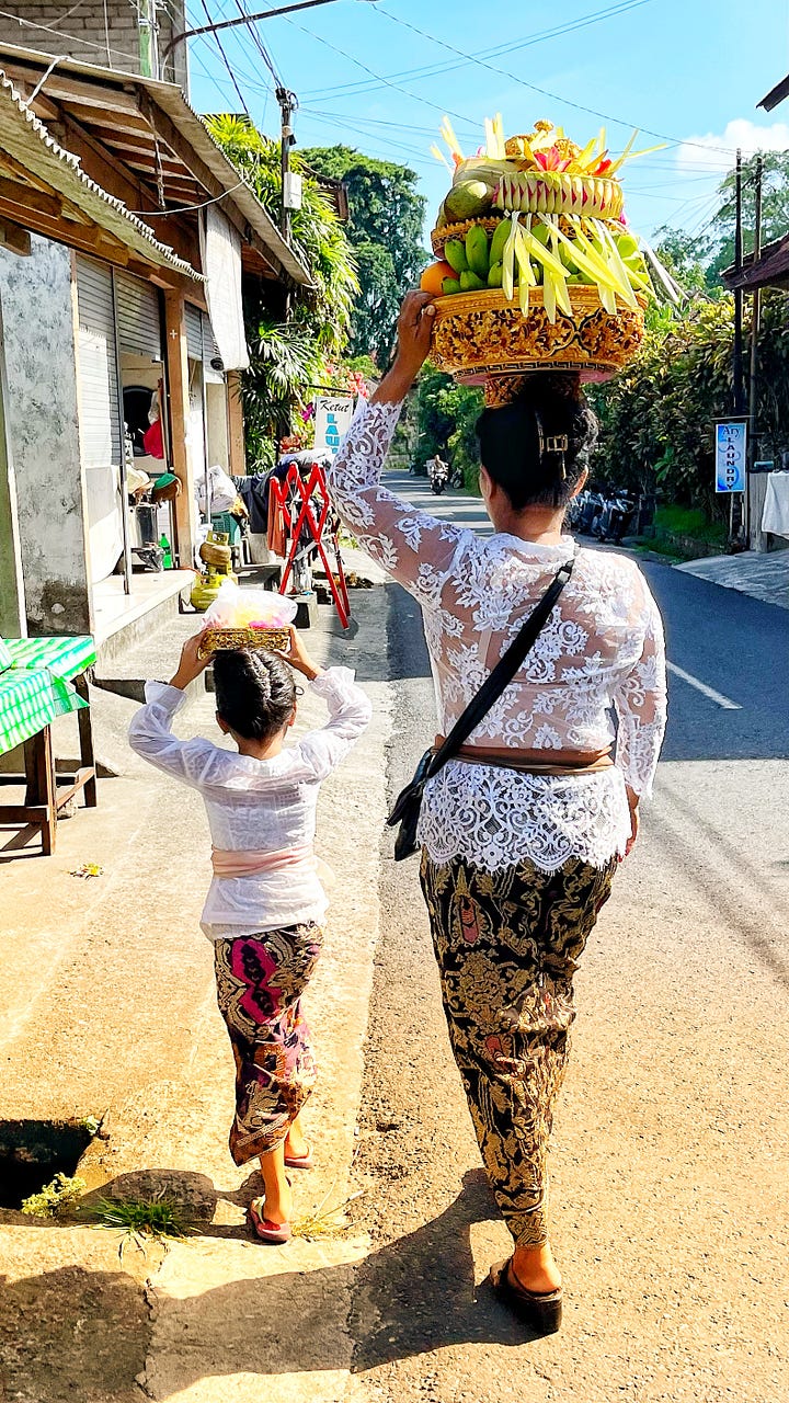 A basket of offerings on the street, and a woman plus her daughter carrying offerings on their heads