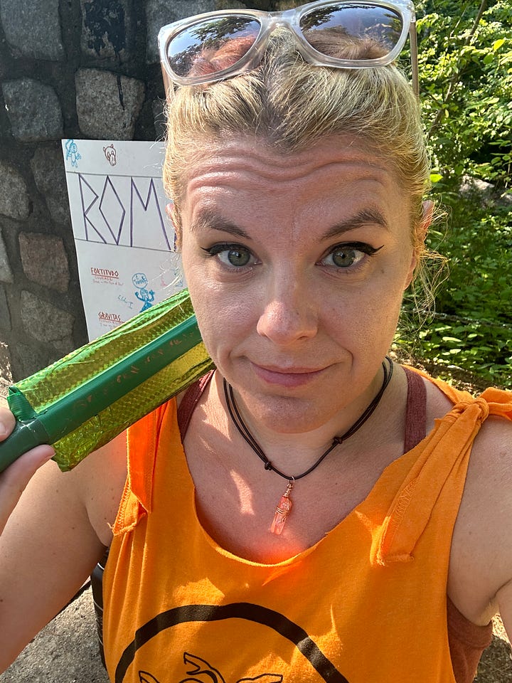 Image One: Airedale Terrier standing on wooden steps above a beach | Image Two: Cass in a green dress, outside | Image Three: Cass in her orange camp t-shirt with her bright green foam sword | Image Four: A large, fiery egg prop festooned with paper chains and wearing a colorful hat