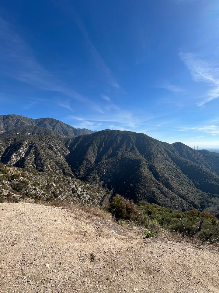 On the right, is a photo of a large green mountain featuring light brown gravel and a clear blue sky. On the right is a view of the Los Angeles skyline featuring a light brown gravel, a clear blue sky but a thick layer of smog in the distance. 