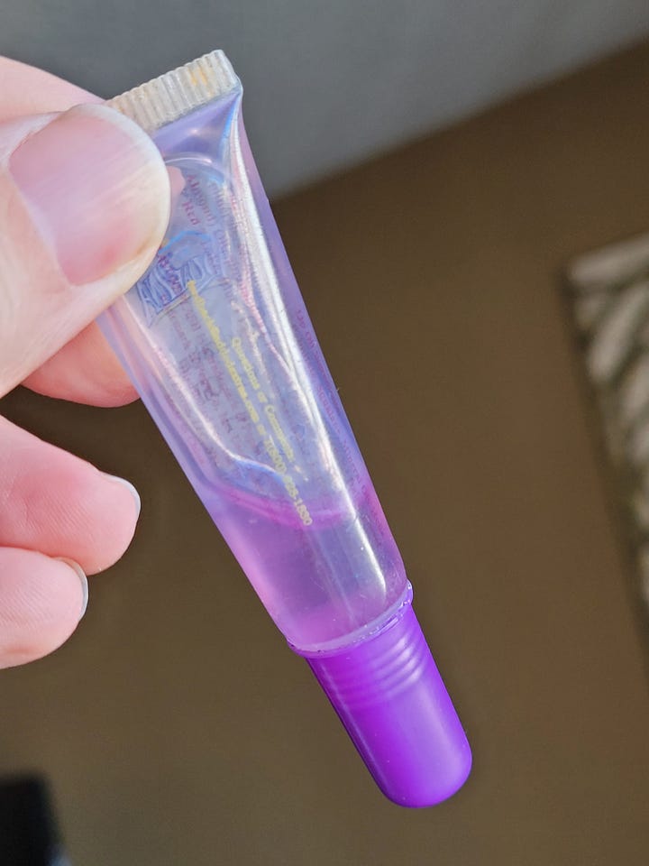 A cheap plastic cup containing granola, milk and a plastic spoon, and a tube of purple lip oil