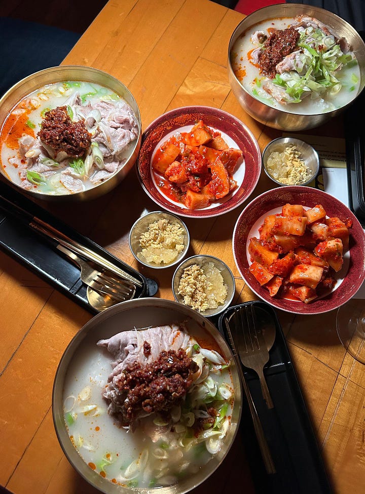Pork gukbap topped with scallions and chili crisp. The full spread of gukbap bowls, kkakdugi (radish kimchi), and sides of fresh ginger and garlic.