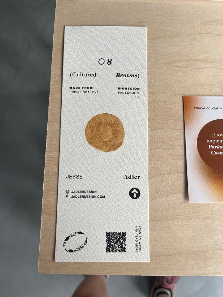 1-2. Exhibition table for 'browns' from Jesse Adler showing part of a mushroom, an eyeshadow made from mushroom pigment and a paint sample of brown fungal dye on paper.
