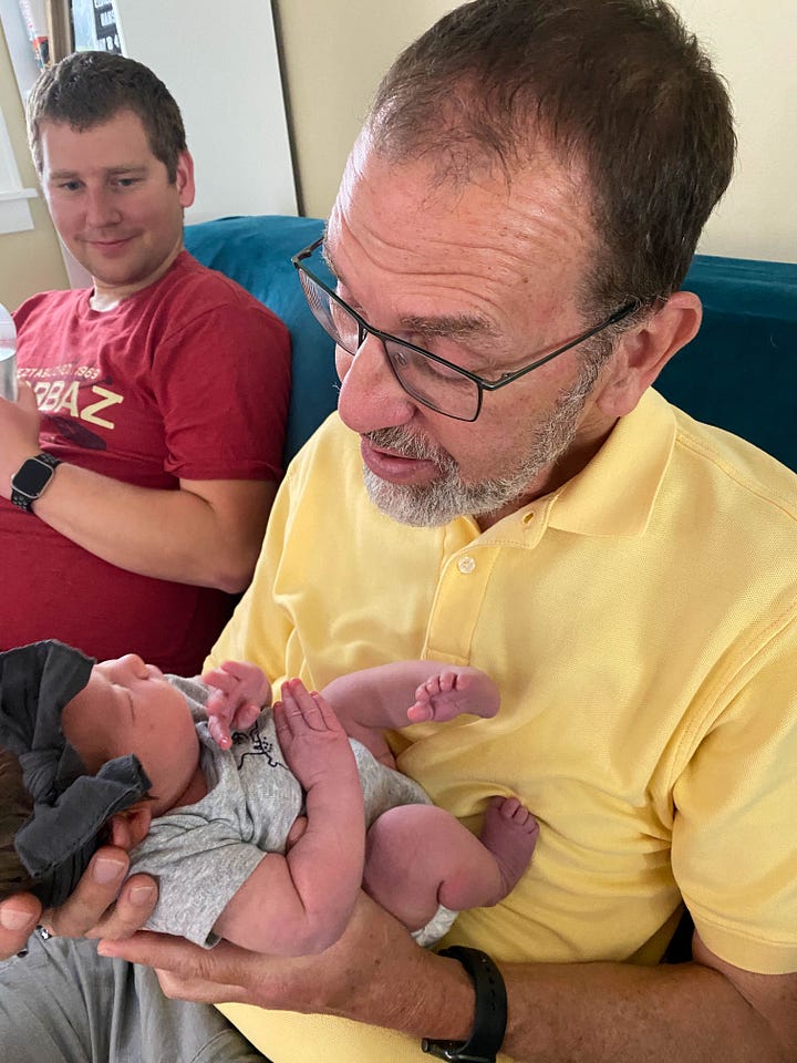 Author holding her new granddaughter. Grandfather (author's husband) holding new granddaughter while the young father looks on.