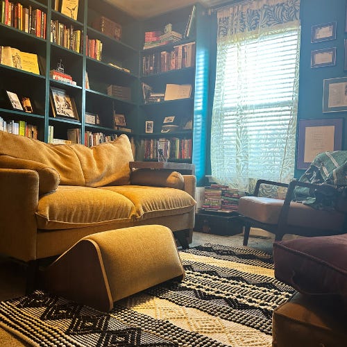 Teal room with bookshelves painted the same color along one wall. The opposite wall contains white open shelves covered in artificial plans and nick-knacks.