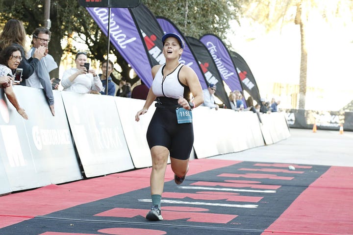 white woman racing toward finish line out of breath, white woman crossing the finish line smiling with arms out to the sides