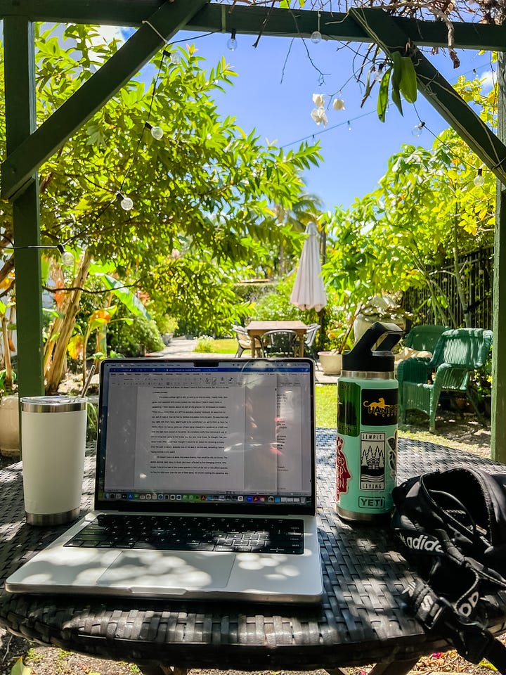 image of a laptop and water bottle and coffee mug and fanny pack on a shaded table beneath a gazebo in a lush garden; image of a two-square-foot beehive alone a black iron fence and green hedge.