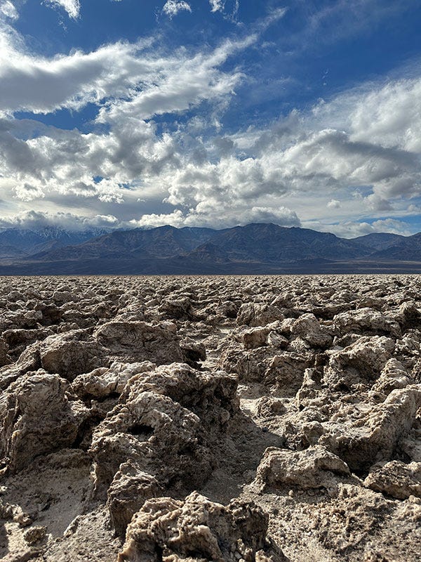 The Devil's Golf Course (heinous salt formations) against a partly cloudy sky with mountains in the distance; a winding butter-colored marble slot canyon, weathered by much flooding.