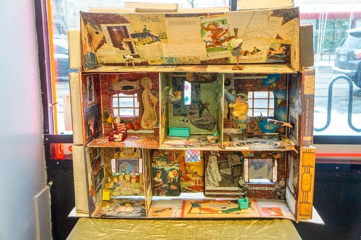 a portable, collapsable dollhouse made with printed images, miniature furniture, cardboard, and fake books.