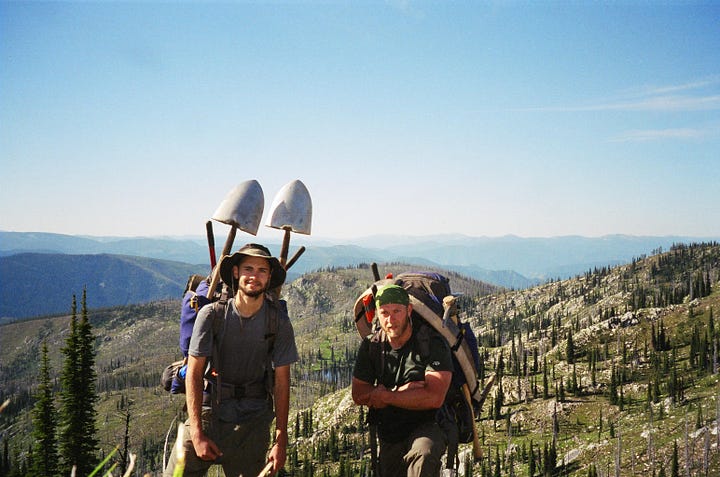 Two men on a mountaintop, a bridge over a creek, a backpack with tools, a waterfall.