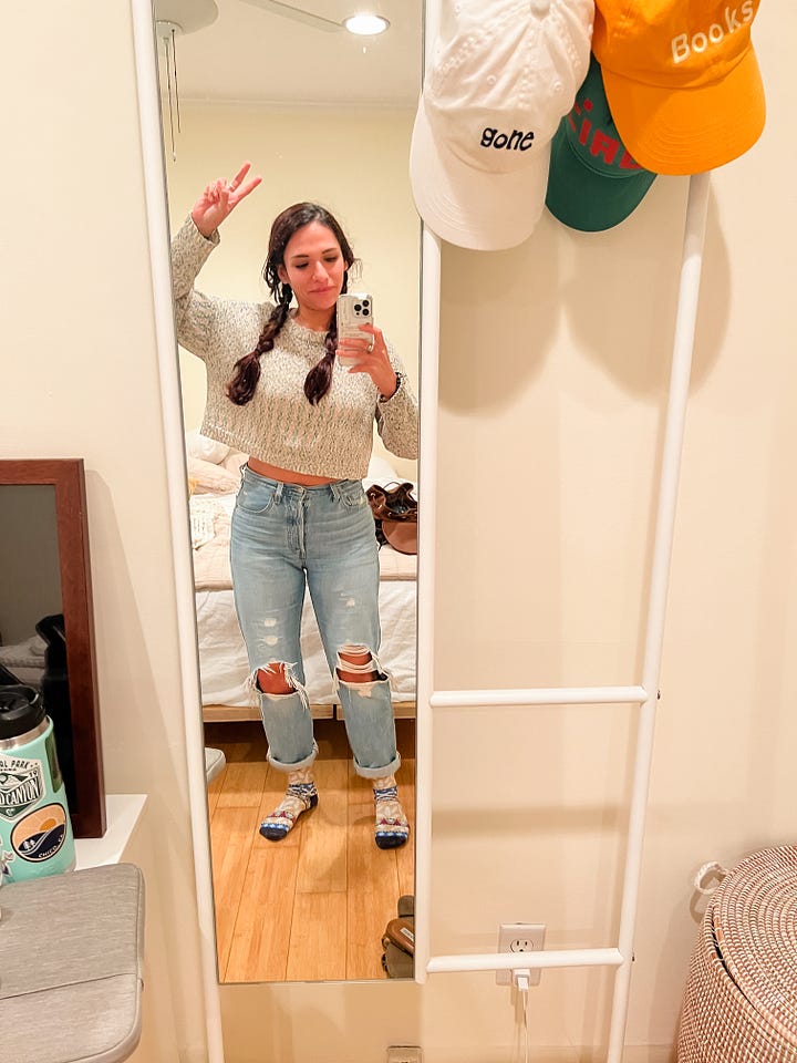 Selfie of woman with laptop behind her, sitting at a kitchen table; mirror selfie photo of woman giving a peace sign with her fingers.