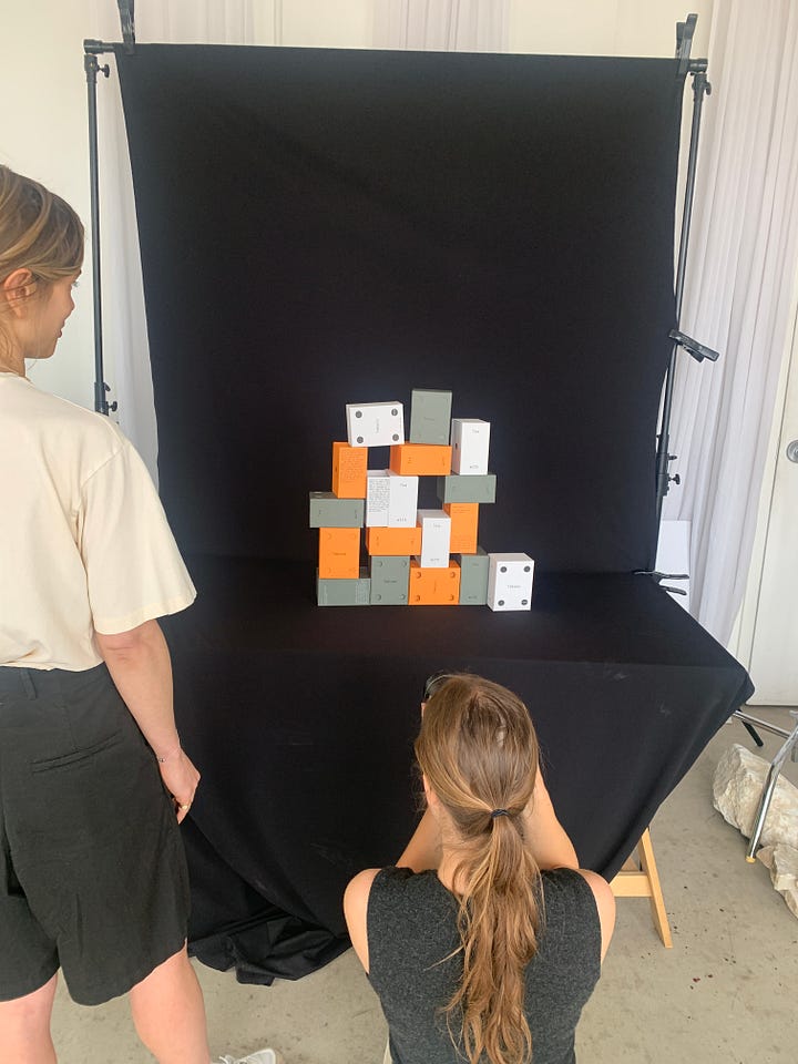 Women photographing boxes of tea on plexiglass and staged backdrops