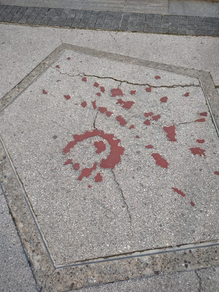 Pictures of a red splotch mark on the ground. It is the indent of a bomb indentation.