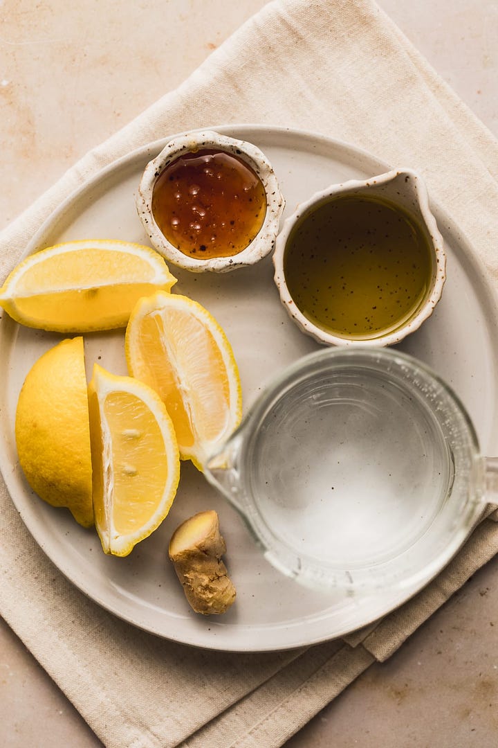 Ingredients for olive oil and lemon drink and a glass of it on a marble surface.