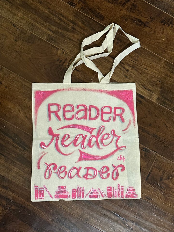 Image 1: A canvas tote which reads "Reader reader reader" in various hand lettered pink fonts and with illustrated books on the bottom; image 2: "Songwriter" hand lettered in pink acrylic paint and surrounded by music notes and a pink microphone; image 3: "Singer" lettered thee times in pink and surrounded by music notes and stars; image 4: "filmmaker" hand lettered in orange with a film strip over the top and a ribbon under the words that read "A Film By Micah Ariel Watson"