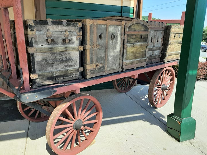 A wagon loaded with old trunks and a closeup of a trunk. The sign for tickets and the chalkboard announcing departures.