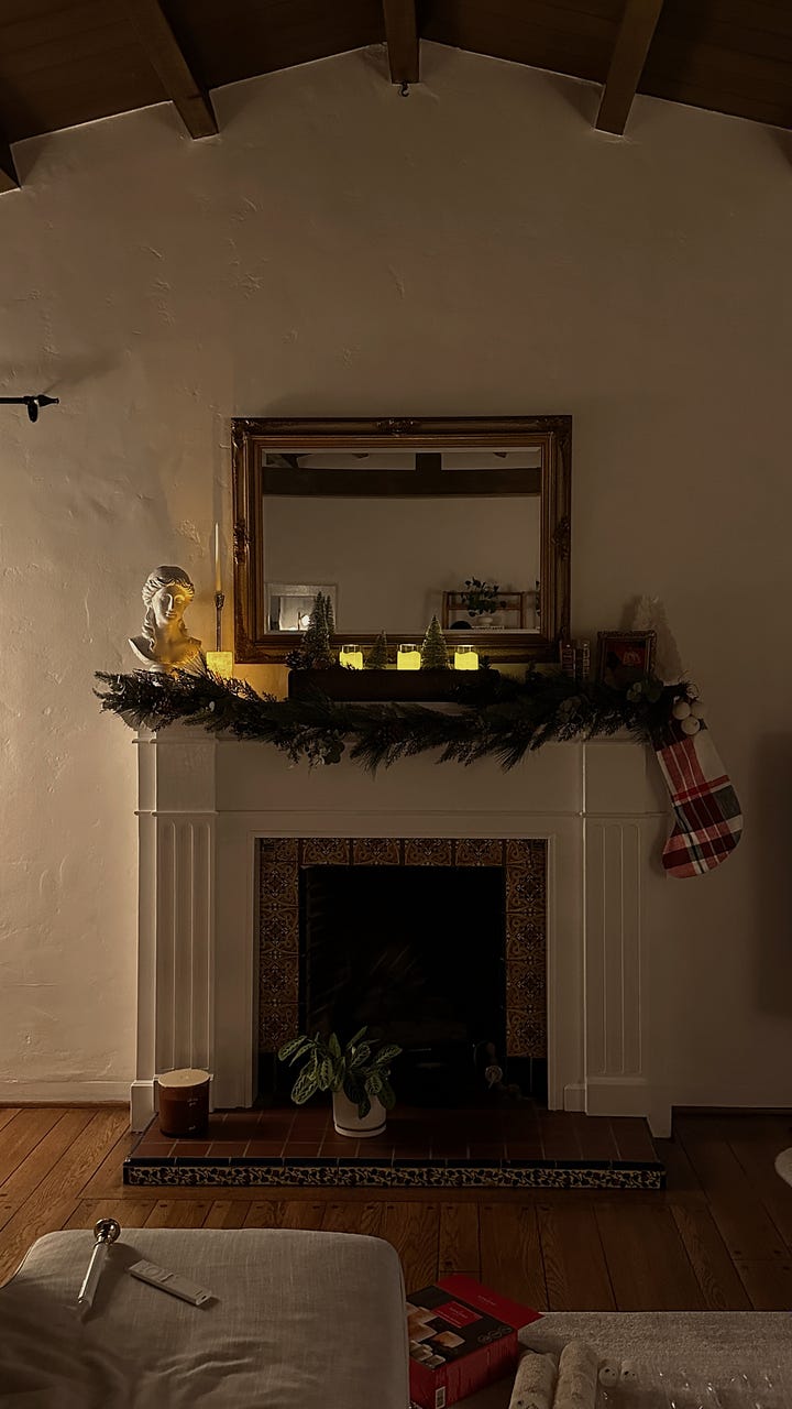 Festively decorated living room featuring garland draping over the mantel, flickering candles, and a single stocking hanging.