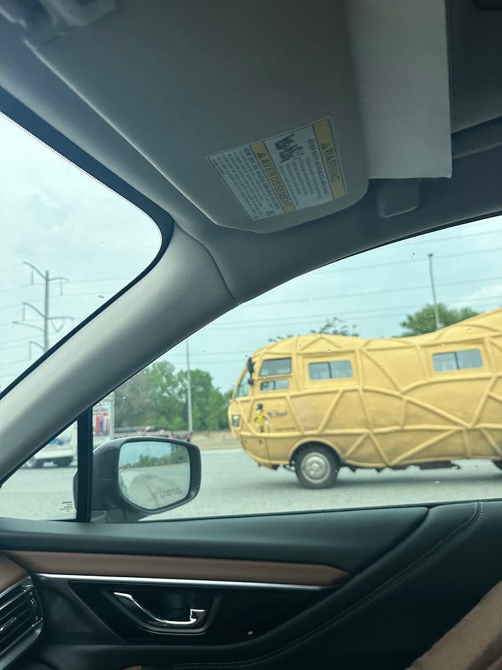 The Planters peanut-mobile, a car shaped like a peanut, is seen through my windshield while driving on the highway.