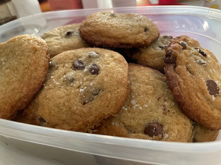 A bowl of very green brothy beans with bread on the side & a tupperware of salty chocolate chip cookies