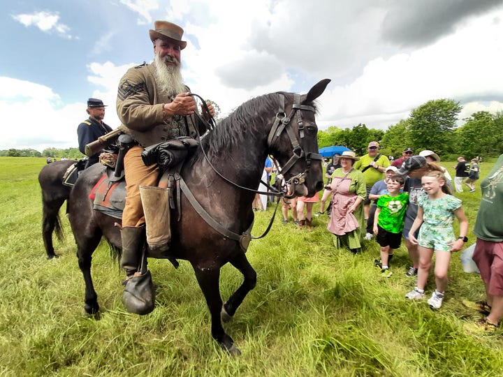 Period dressed riders on horses stand close to the cord, answering questions.