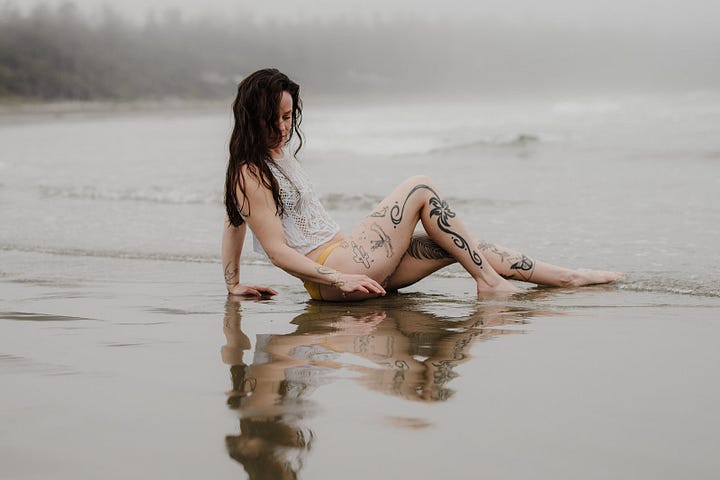 Beach front Tofino arranged photo shoot A couple posing on the rock, Videographer Brittany Ballamy running in the sand, surfer Emily Ballard sitting on the beach and a women in Reclamation company dress posing on rocks over looking the water 