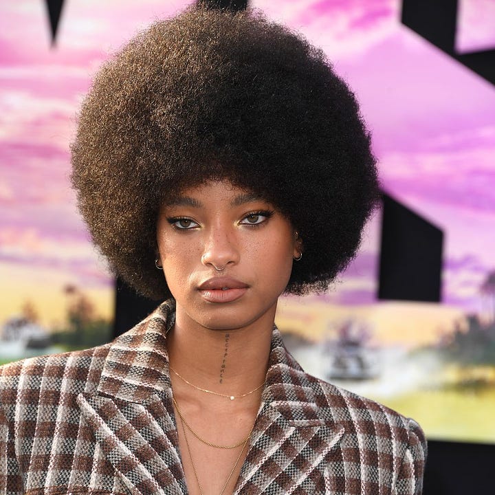 Willow Smith poses with an Afro. In one photo, she is wearing a plaid jacket during a red carpet appearance. In the second photo, she smiles widely with grills on her teeth for the empathogen album cover.