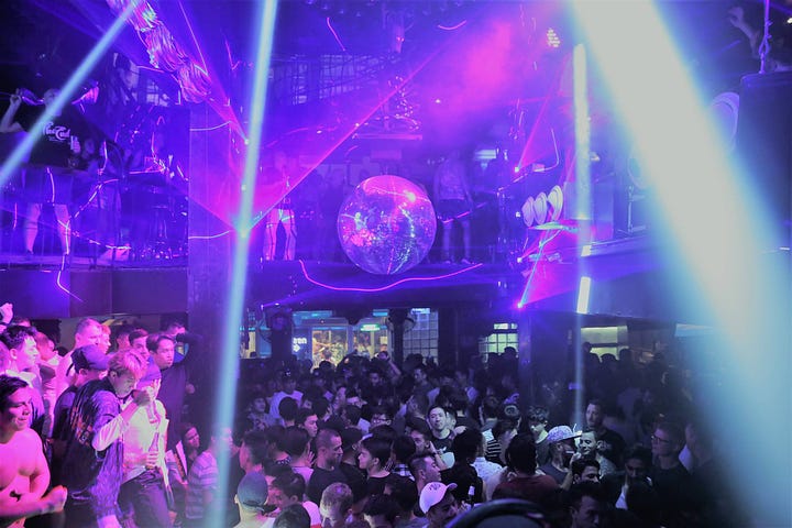 Revelers dance under the discoball at the crowded  DJ Station. Two queer women  with eccentric makeup pose at Go Grrls.