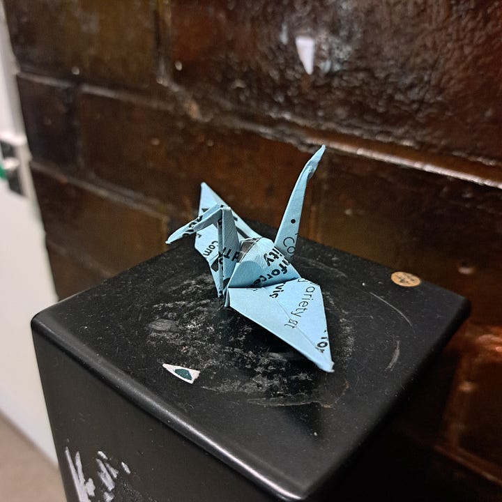 paper cranes folded from some sort of informational pamphlet and positioned on a random, beat up black post