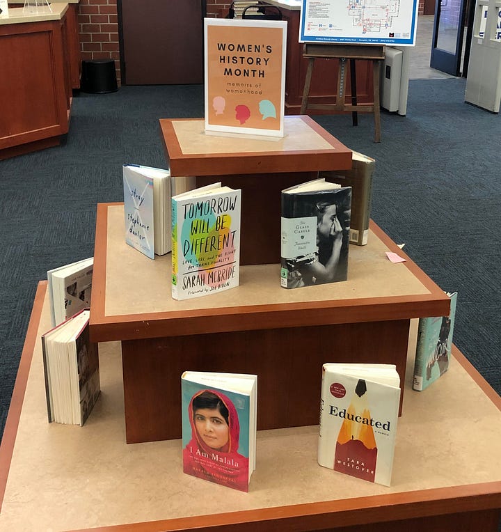 First image is a book display for women's history month featuring memoirs from female authors and the second is Marty posing next to a book display with the title "Good Books make winter bearable" with a plush bear posed nearby.