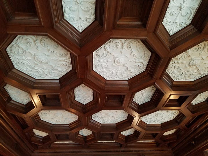 A room with an ornate wood ceiling, wooden walls and fireplace, with a closeup of the ceiling.