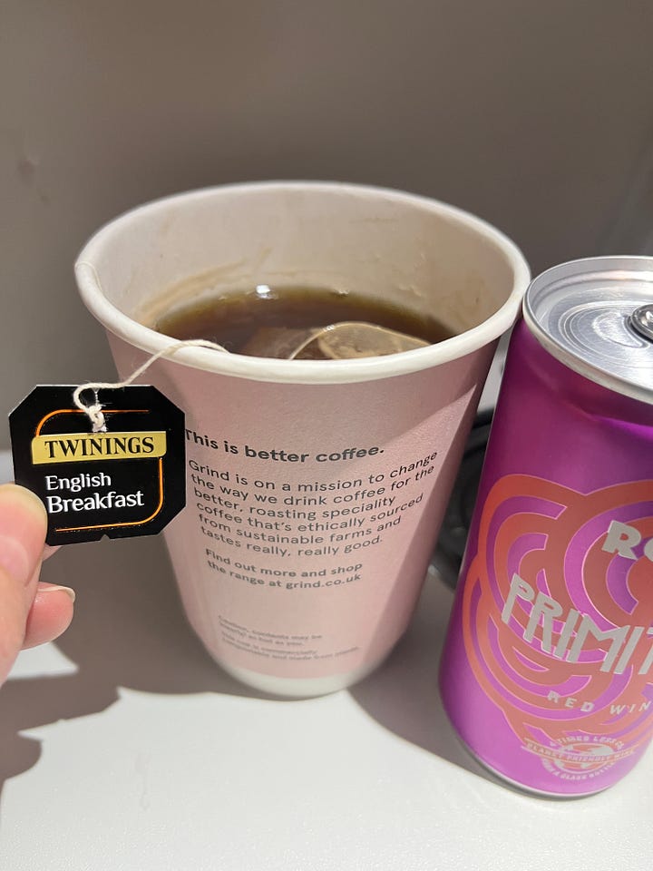 Image 1: H&E on the plane smiling at the camera. Both white with brown/grey hair. Photo of a cup of tea & a tin of red wine on a flight table