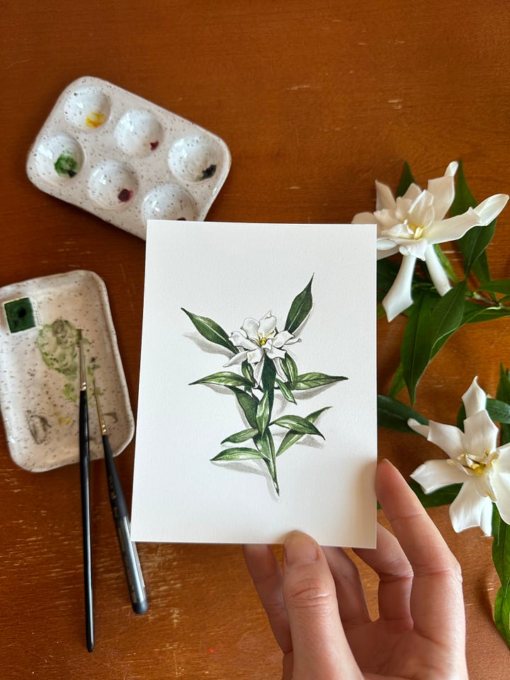 a small painting of a red chili pepper with paintbrush and palette close by, and a painting of a single gardenia flower with real gardenia flowers next to it 